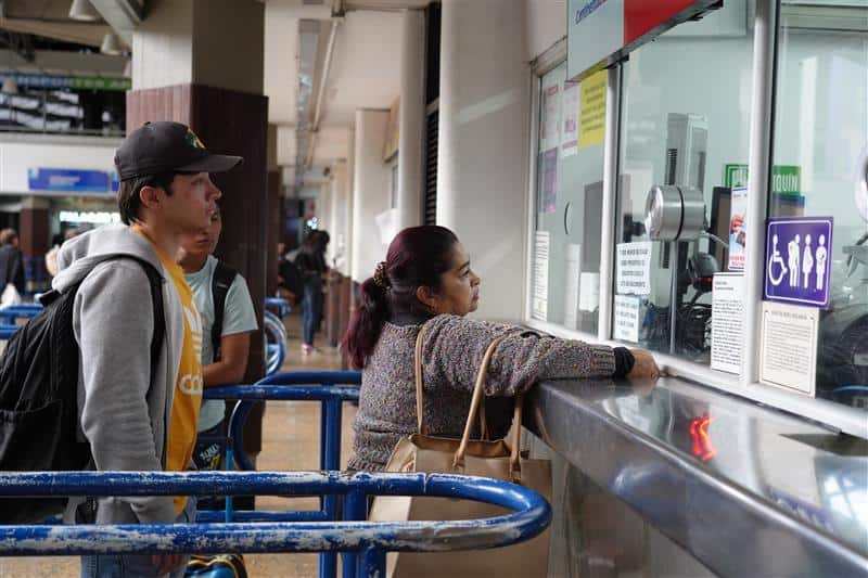 Personas realizan consulta en taquilla de transporte en una terminal, frente a ventanilla de atención.