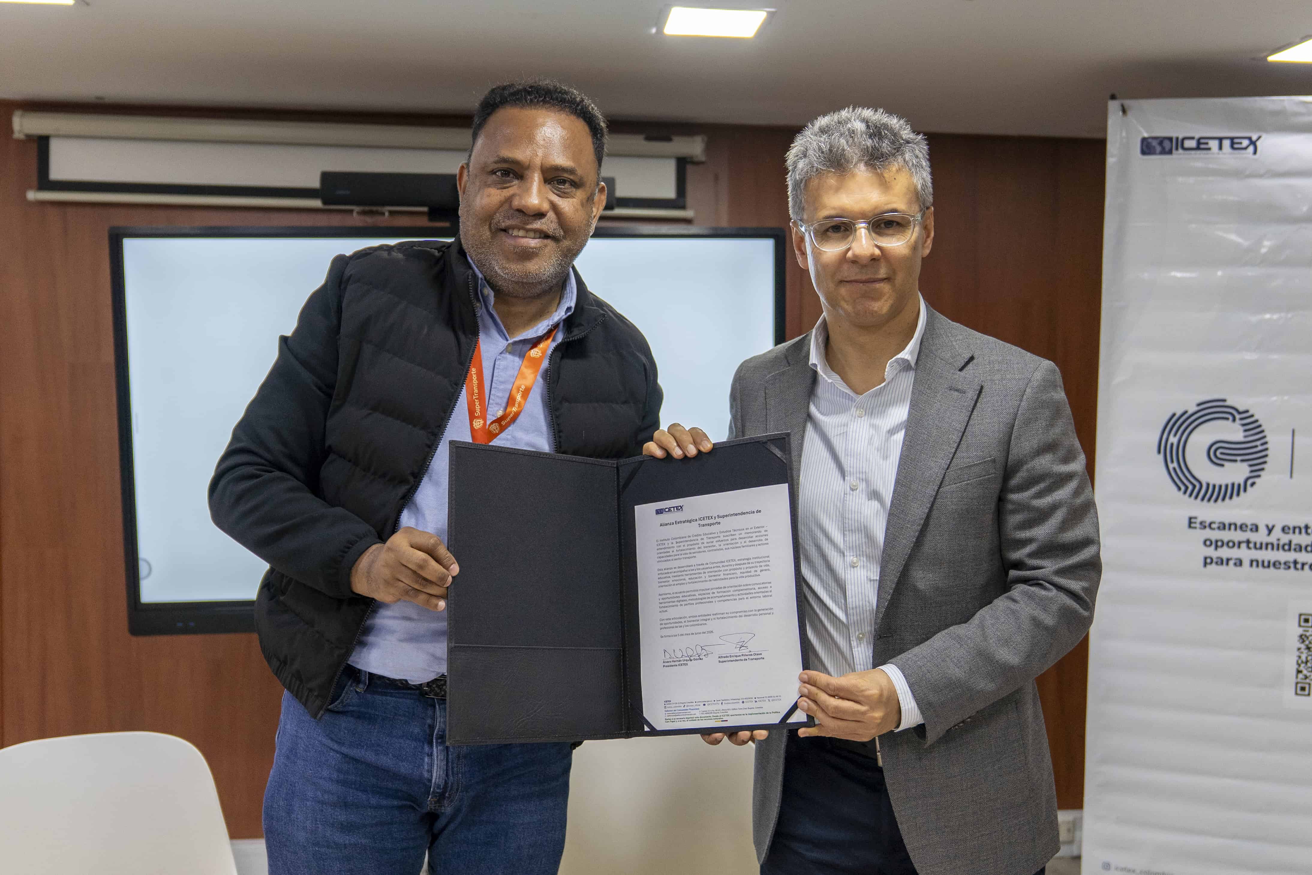 Dos personas sostienen un documento firmado durante un acto institucional en una oficina.
