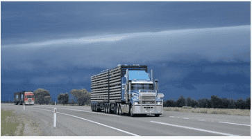 Camión de carga circulando por una carretera rural bajo un cielo con nubes oscuras de tormenta. Imagen utilizada para ilustrar un comunicado relacionado con transporte o condiciones climáticas.