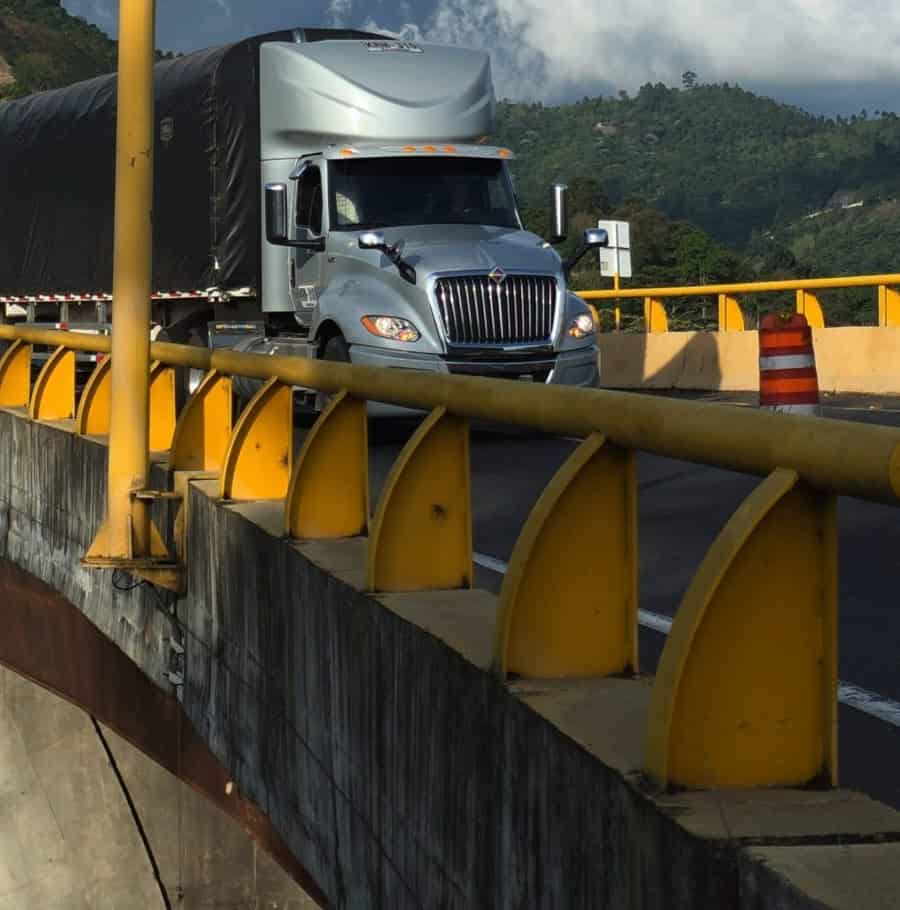 Camión de carga transita por un puente vial en una carretera de montaña, representando el transporte de carga por carretera en Colombia.