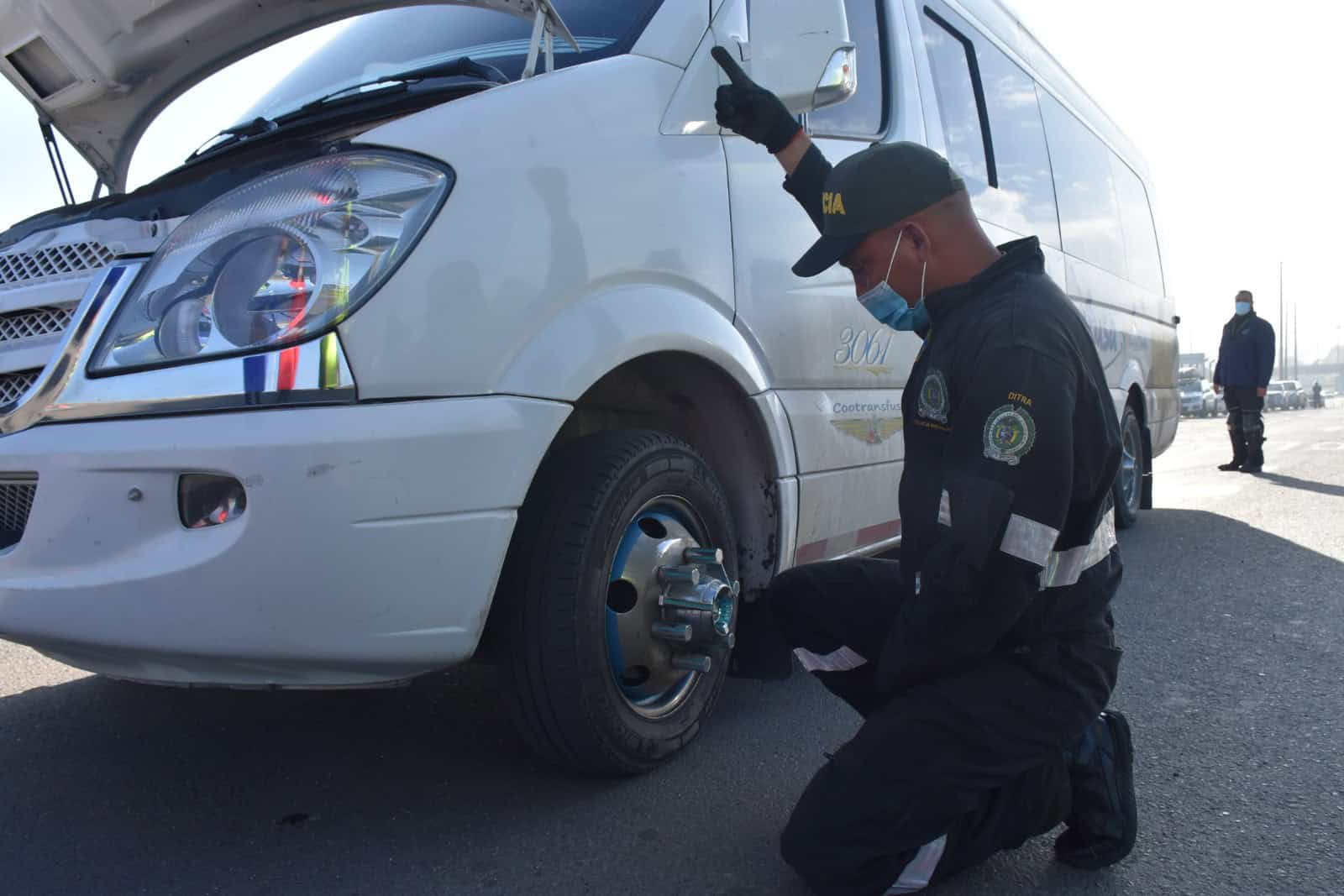 Inspección de seguridad a un microbús de transporte en vía pública, con revisión de llantas y condiciones mecánicas del vehículo.