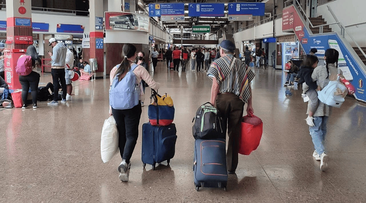 Viajeros con equipaje se desplazan por el interior de una terminal de transporte.