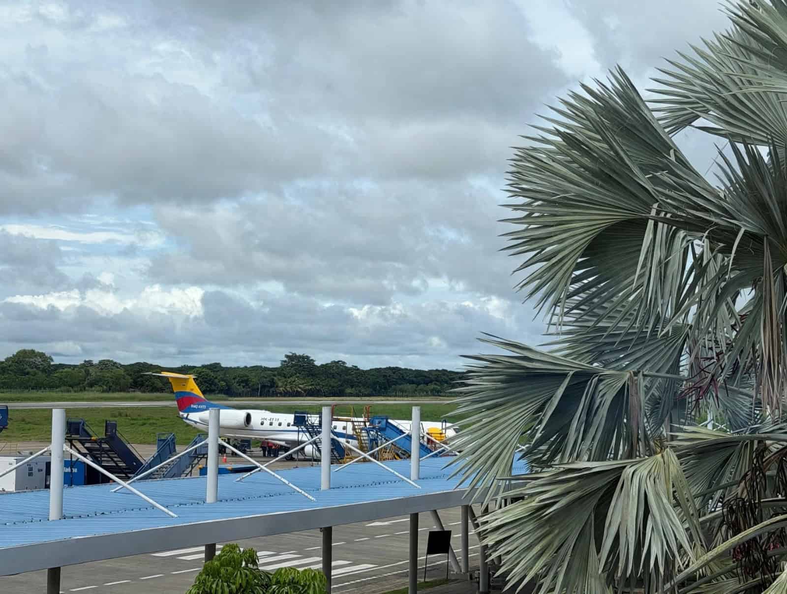 Aeronave de matrícula colombiana estacionada en la pista del aeropuerto de Montería, con escalerillas de abordaje, vegetación tropical y cielo nublado de fondo.